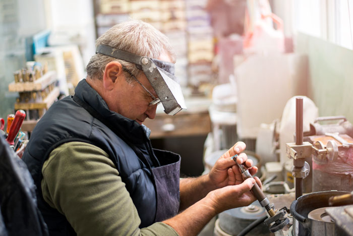 elderly man wearing eyeglasses and magnifying glass sitting at work bench tinkering with tools